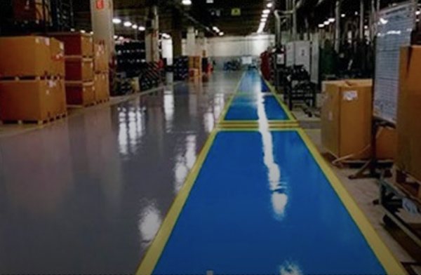 Piso industrial revestido em epóxi dentro de um centro de distribuição, com corredor demarcado em azul e faixas amarelas