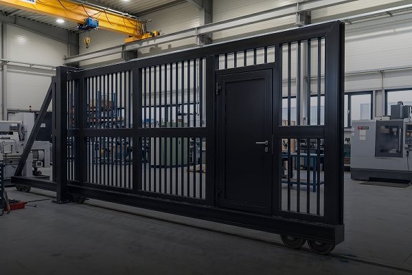 Portão metálico industrial de grande porte com acabamento em esmalte sintético preto, dentro de um galpão de serralheria